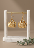 Gold woven basket earrings on a marble stand with a beige background